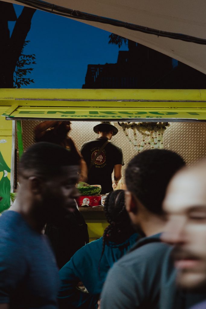 a picture of a yellow food truck with people queuing in front of it