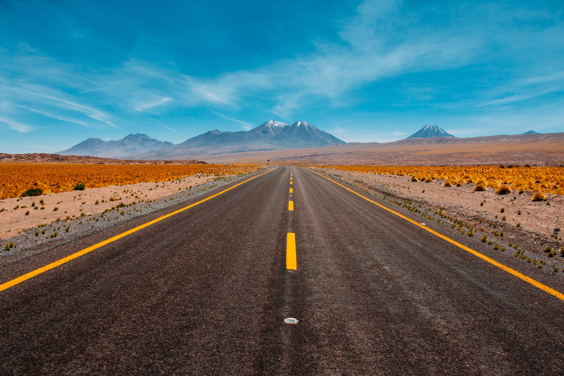 Picture of a vast landscape with a road leading ahead. Mountains and blue sky in the background