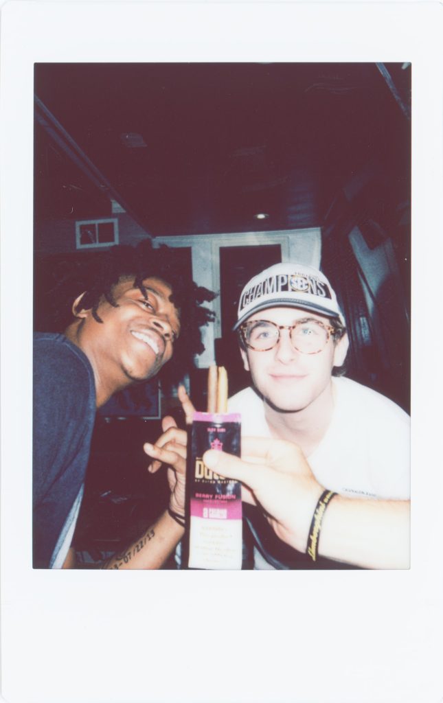 Polaroid image of two males. One wearing a black top another wearing a white top with glasses and a cap