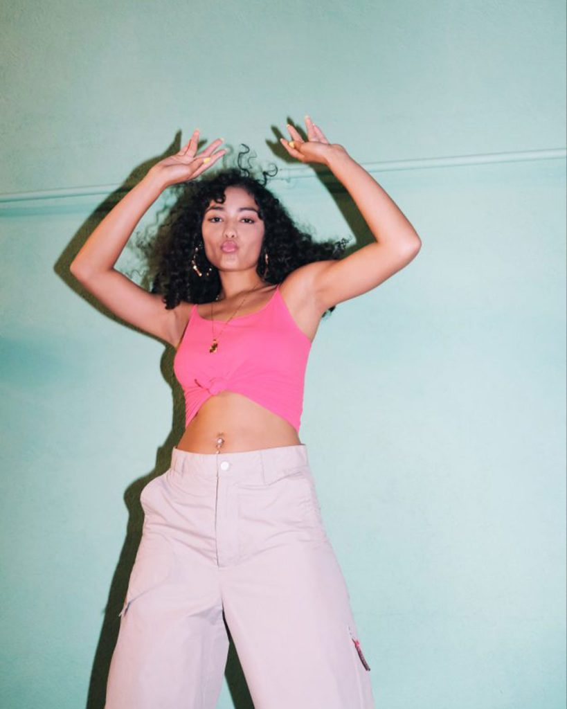 Black female with dark curly hair posing in a pink outfit