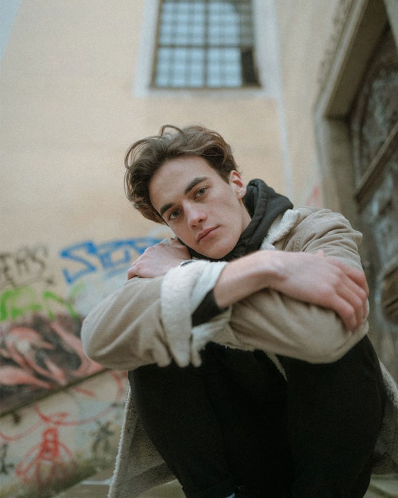 Caucasian male crossed arms wearing cream jumpers and black trousers 