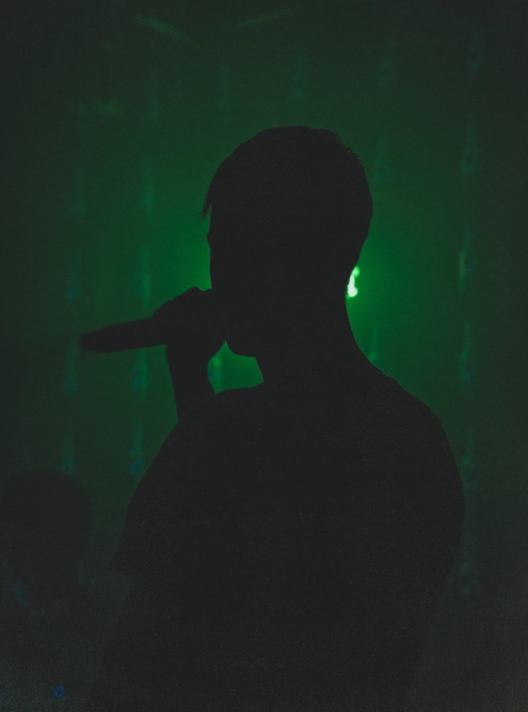 A dark silhouette holding a microphone with a green lit background.