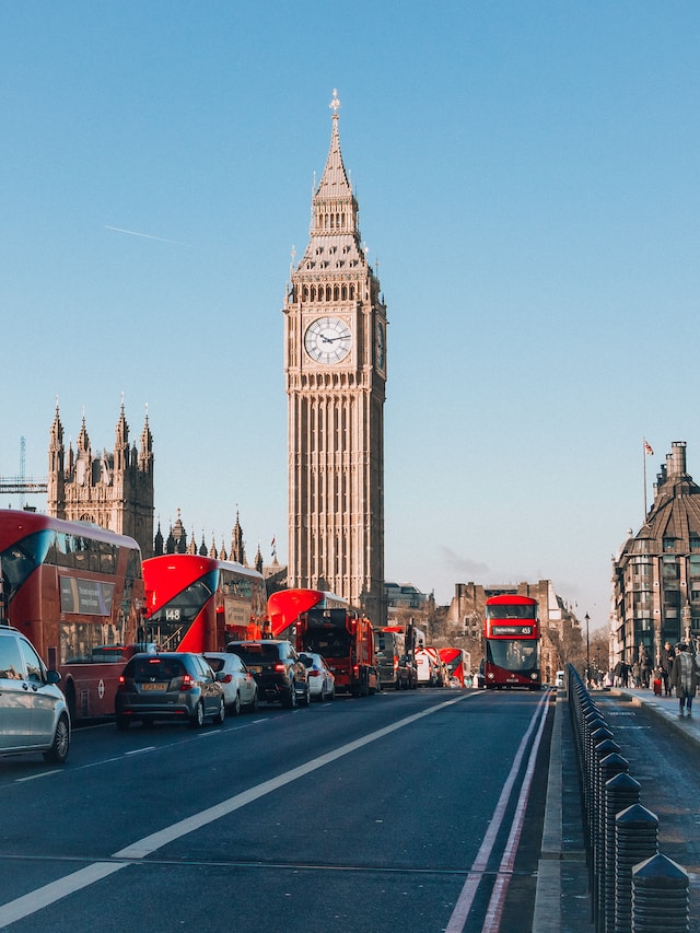 A picture of Big Ben on sunny day. Double decker red busses and traffic in front of it